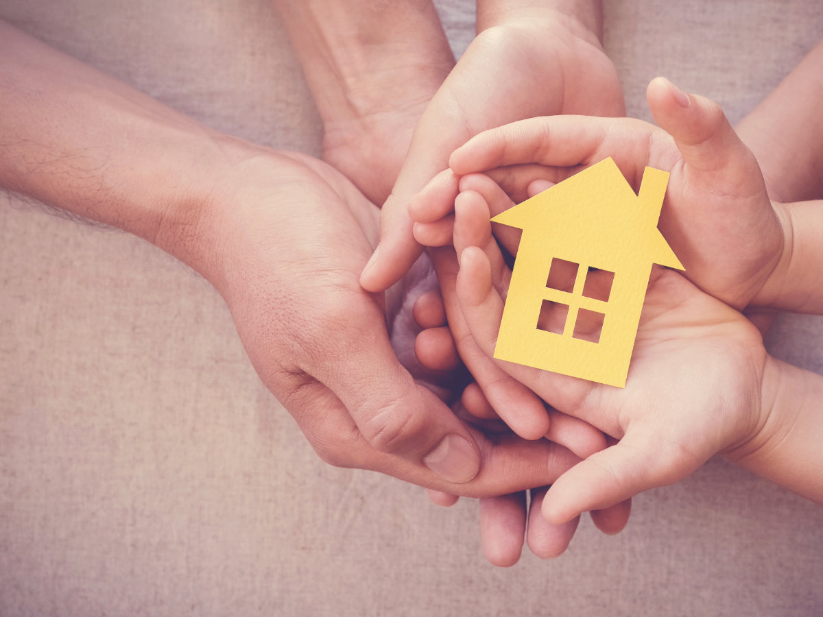 Hands of a family holding a yellow house cutout, symbolizing trust, unity, and at-home DNA testing with My Forever DNA.