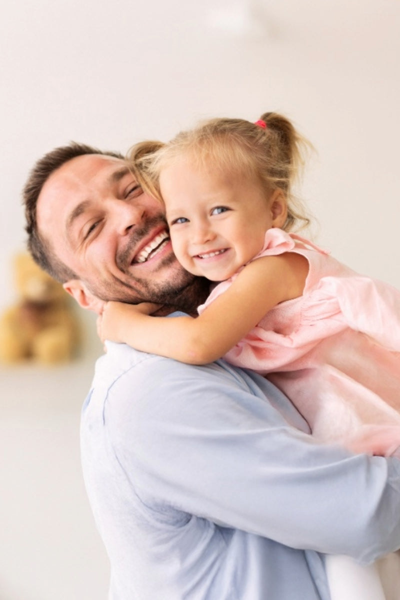Man holding a young girl in a pink dress against a light background